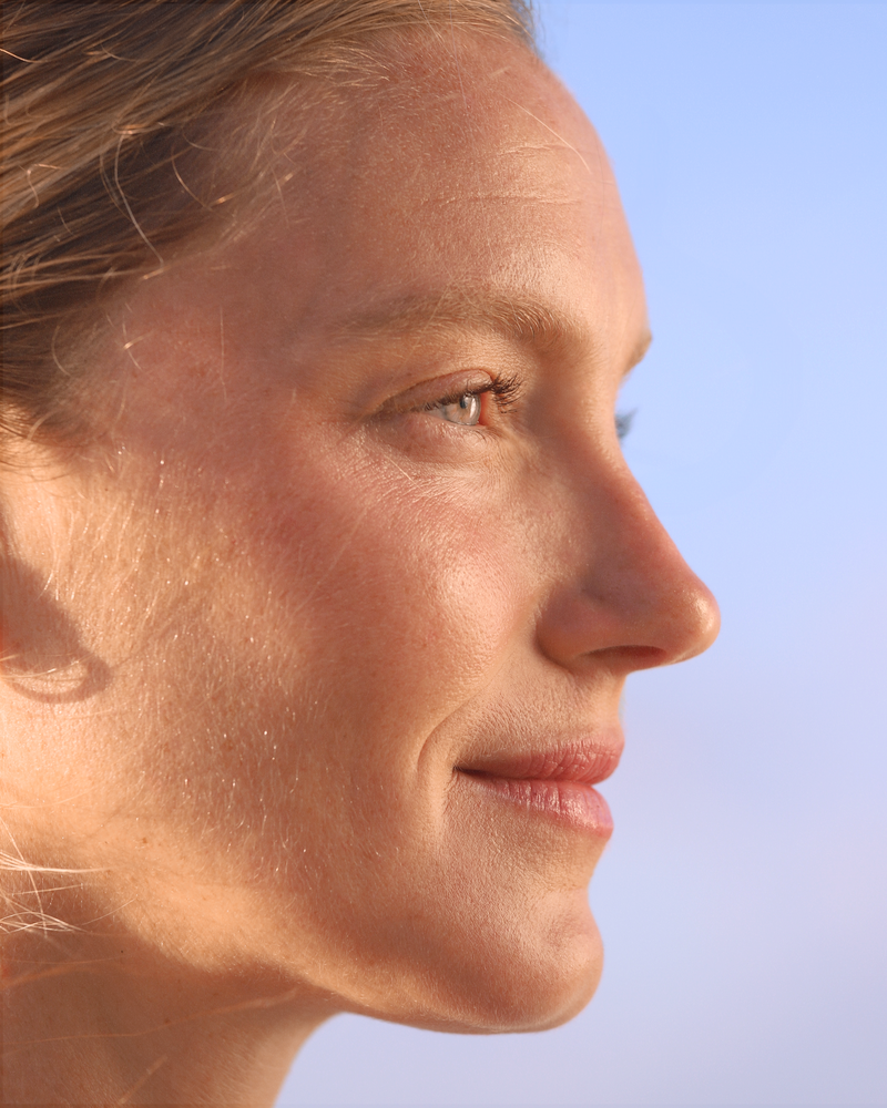 Sunlit close-up profile portrait of a woman against a soft blue sky