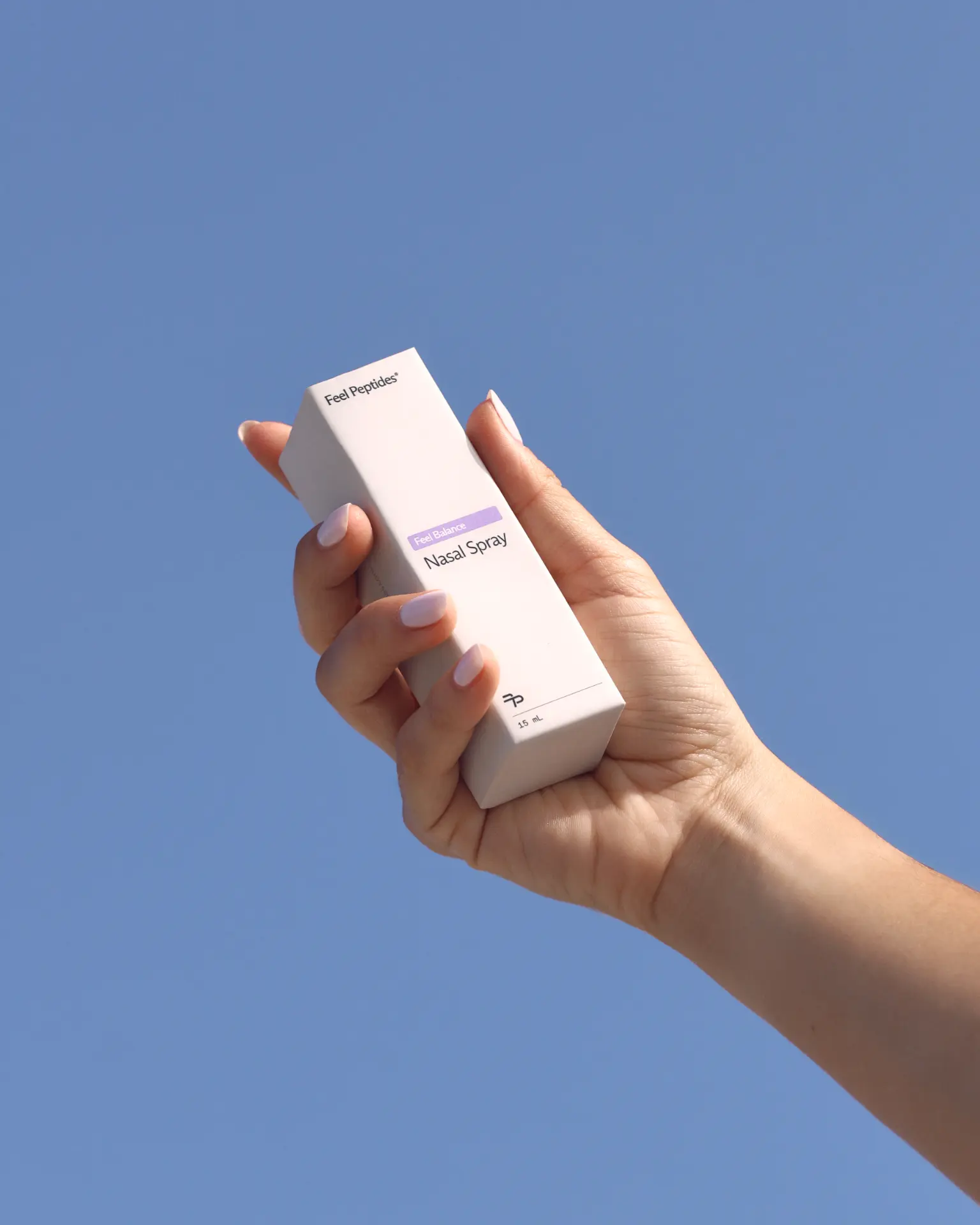 Hand holding a Feel Balance nasal spray box against a blue sky